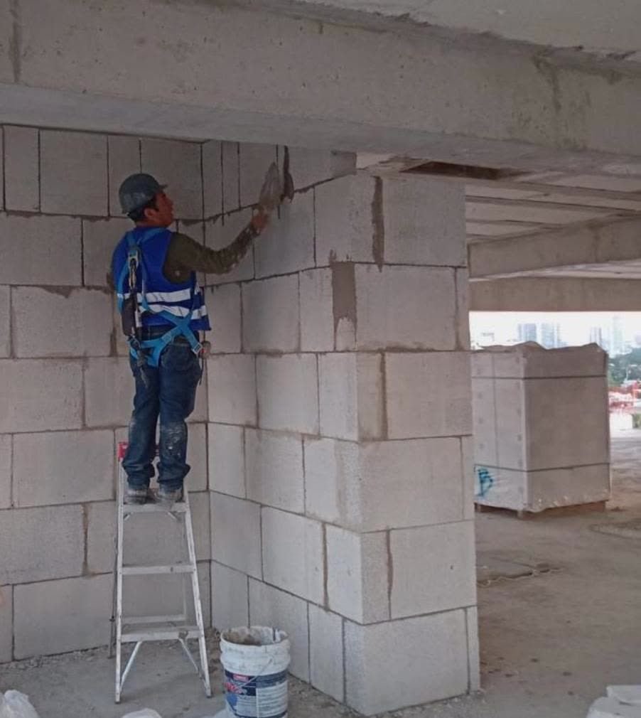 Trabajador aplicando acabado sobre un muro de bloques.